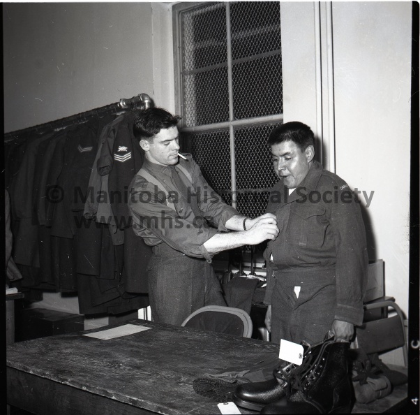 TRY THIS FOR SIZE - A new recruit for the local militia unit, F. Myaran of Rossendale, gets fitted for his uniform. L/Bdr. R. Hayter of the unit's quartermaster stores does the fitting chore. The unit strength has increased by more than 50 in recent weeks. 1354.jpg