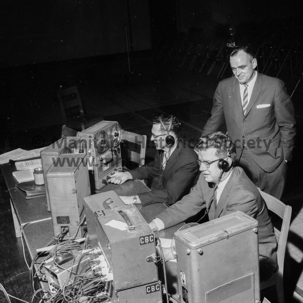 Photographer: Tashiro
October 25, 1963
Educational
Portage Collegiate foursome battle Neepawa group in CBC’s national “Issues and Answers.”
It took two technicians to run the CBC’s Issues and Answers program held at the Portage Collegiate on Friday afternoon. Here announcer Bob Burron stands over Ernie Brown and Larry Nilson, front, as they adjust the recording equipment. VP-1-00602-004.jpg