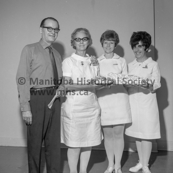 Photographer: Tashiro
June 12, 1970
Retirement
Mrs. R. L. Cochran R.N. retires from hospital staff
After almost 16 years of service at the Portage General Hospital, Mrs. R. L. Cochran, RN, is retiring from the permanent staff. Mrs. Cochran joined the staff in September, 1954. She worked as general duty RN on surgical and was day supervisor for nine months. She returned to general duty and moved to central supply in July, 1956 and has been there since. She will continue to serve on a part-time basis. Special presentations and a farewell cake marked her retirement during the staff coffee break Friday afternoon in the hospital cafeteria. In the photo, from the left, Alderman A. R. Barrett who made a presentation of an engraved silver bracelet on behalf of the board of directors of the hospital, Mrs. Cochran, Carole Hancock, R.N., day supervisor holding the cake and Tanis Dreher, R.N., who made the presentation of a silver brooch and matching earrings on behalf of the hospital staff. VP-1-00974-001.jpg