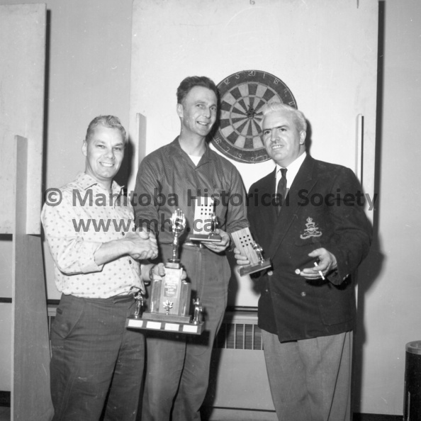 Photographer: Moffat
April 7, 1963
Can. Legion
Canadian Legion dart tournament and winners
Champion dart throwers in the Portage branch of the Royal Canadian Legion are Vic Dyer and Ken Holland, seen here at extreme right, as they receive the branch trophy and miniatures from sports committee chairman Cliff Steeden. The playoff was held during the weekend, the first competition for the new trophy. The pair won over some 20 teams entered in the event. VP-1-01227-002.jpg